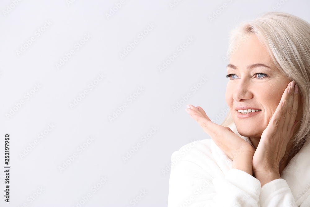 Mature woman giving herself face massage on light background - obrazy, fototapety, plakaty 