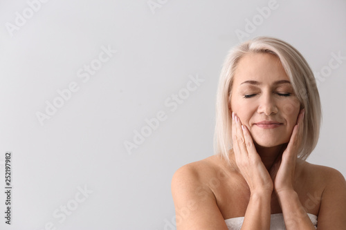 Papier peint Mature woman giving herself face massage on light background