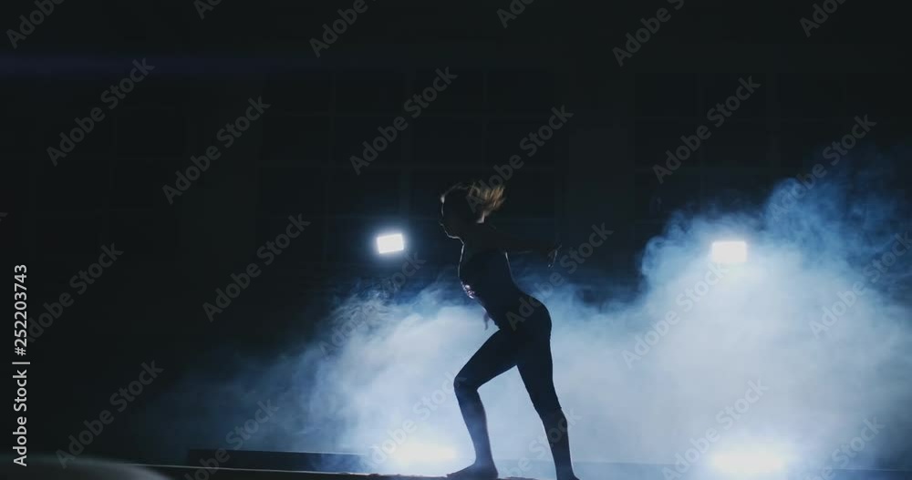 Side view of a female gymnast doing split handstand on balance beam against black background. Side view of a female gymnast doing split handstand on balance beam against black background.