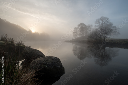 Sunrise on a misty morning over the River Brathay, between Elterwater and Skelwith Bridge. Trees reflected in the water. Lake District, UK photo