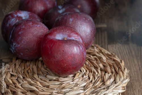 Top view of plums on esparto base and wooden background