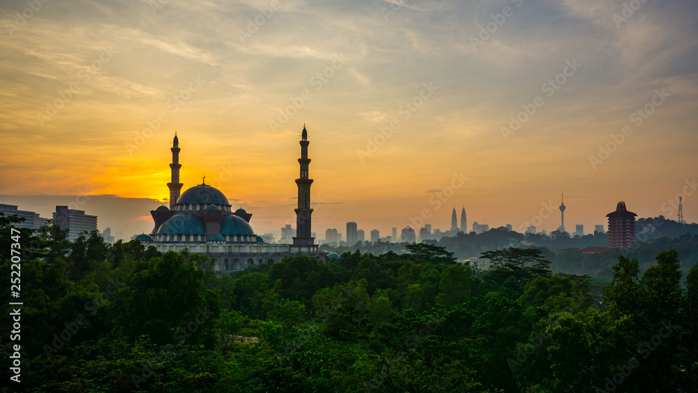 The Federal Territory Mosque during sunrise with Kuala Lumpur city skyline on the background.