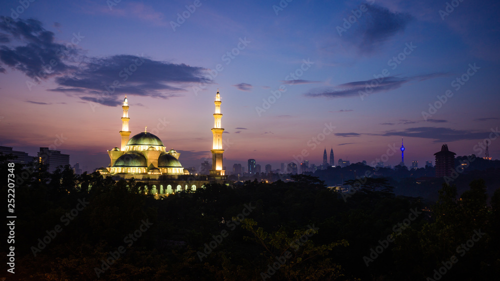 The Federal Territory Mosque during sunrise with Kuala Lumpur city skyline on the background.