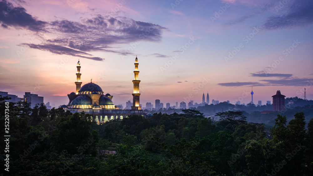 The Federal Territory Mosque during sunrise with Kuala Lumpur city skyline on the background.