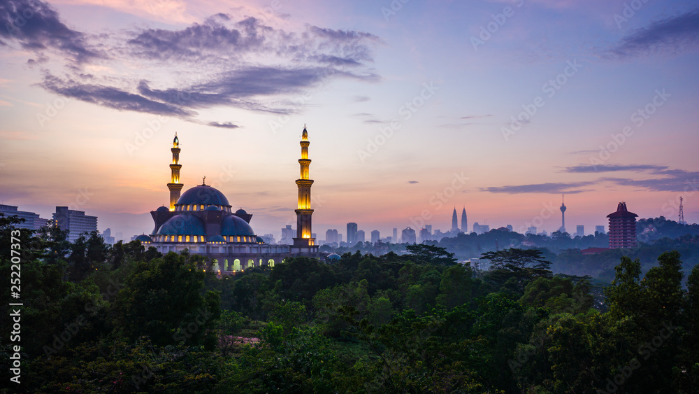 The Federal Territory Mosque during sunrise with Kuala Lumpur city skyline on the background.