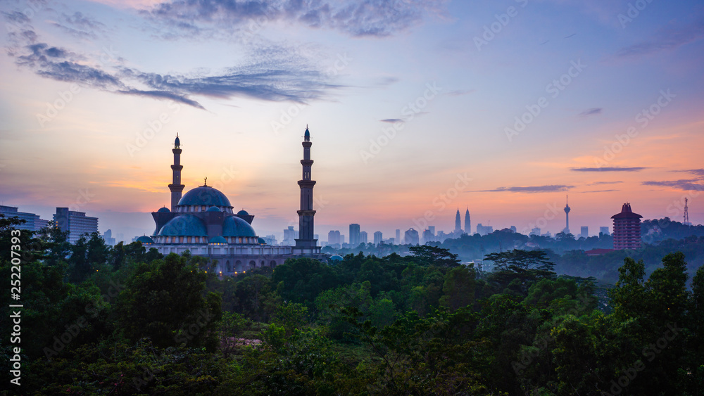 The Federal Territory Mosque during sunrise with Kuala Lumpur city skyline on the background.
