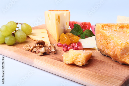 Assortment of cheese with fruits, grapes, nuts and cheese knife on a wooden serving tray. photo