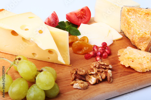 Assortment of cheese with fruits, grapes, nuts and cheese knife on a wooden serving tray.