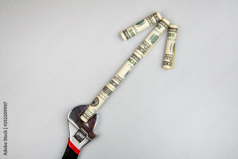 Concept of fixing currency of money and tools. Wrench and dollars on a gray background. Money is an arrow
