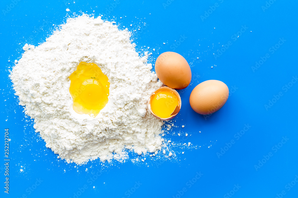 Making dough concept. Pile of flour and eggs on blue background top view Making dough concept. Pile of flour and eggs on blue background top view