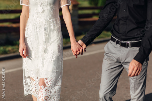 Cropped photo young lovers married couple, husband and wife, held of hands walk along the street. lower half. Close Up