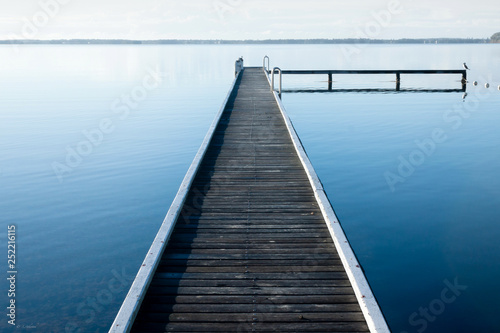 Calm lake with wooden jetty and light fog on horizon