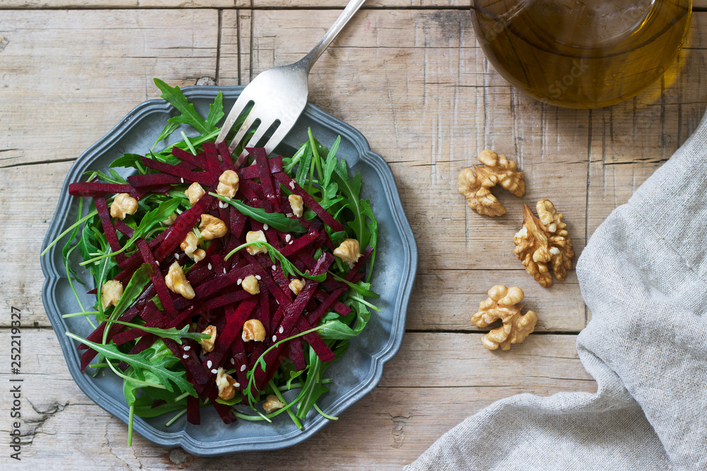 Vitamin salad of raw beets, arugula, walnuts and olive oil on a wooden table. Rustic style.