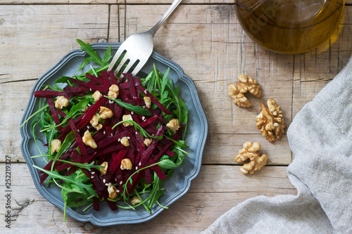 Vitamin salad of raw beets, arugula, walnuts and olive oil on a wooden table. Rustic style.