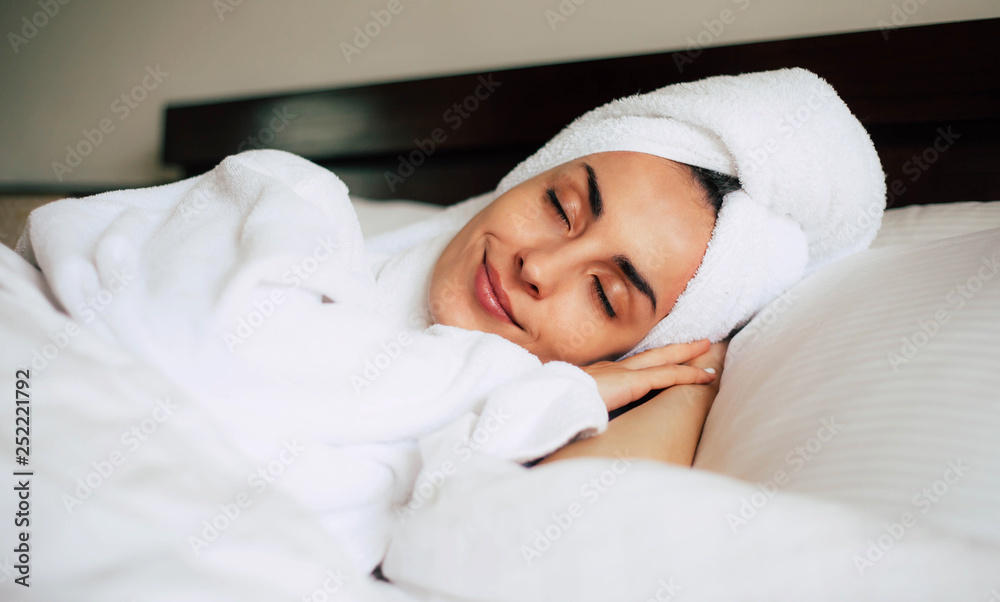 Middle day nap. Cute young girl is having a relaxing nap after shower in cozy double bed with bright white bedclothes. Her skin is tanned, eyebrows are nicely shaped and her smile is pleasant.