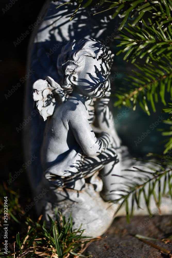 A sandstone sculpture of an angel covered with shadows of pine needles. A sandstone sculpture of an angel covered with shadows of pine needles.