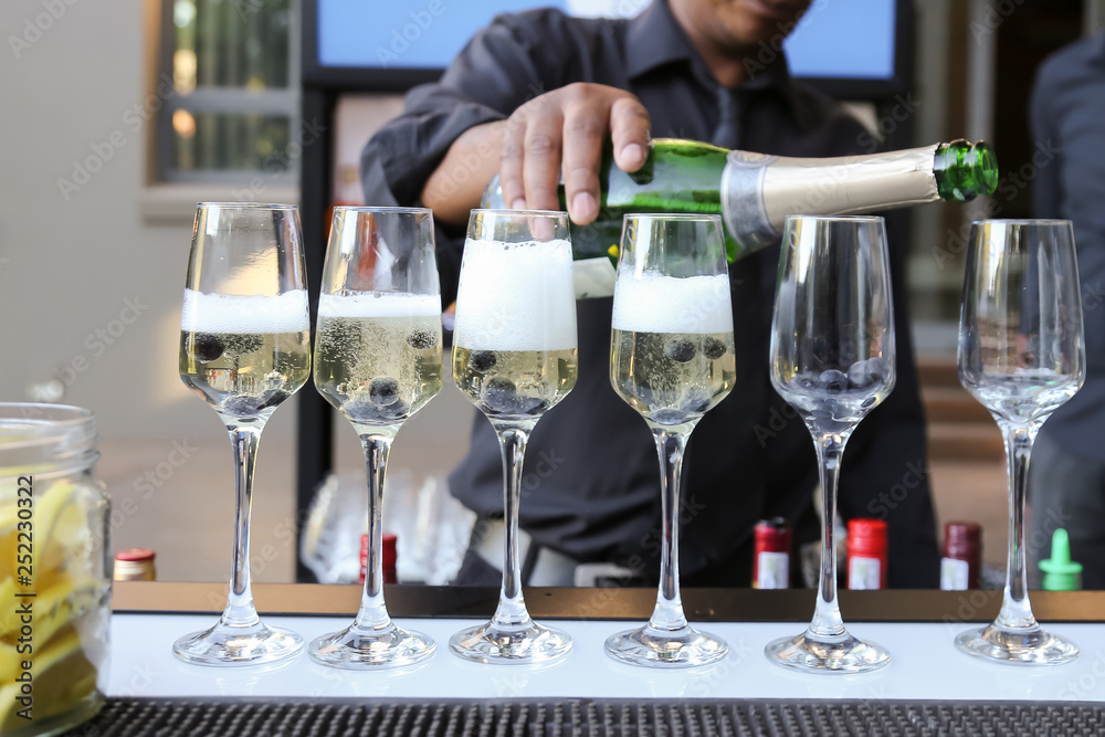 barman pouring champaign in six glasses with blue berries