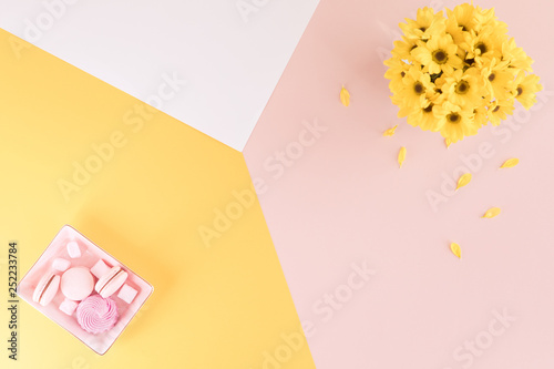 Summer flatlay composition. Yellow flowers on pastel yellow pink and white mu...
