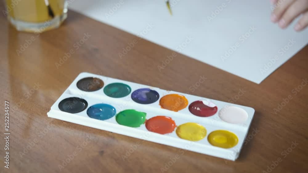 Hands of a child with paints. Top view of a child drawing with a brush and paints. Hands of a child with paints. Top view of a child drawing with a brush and paints.