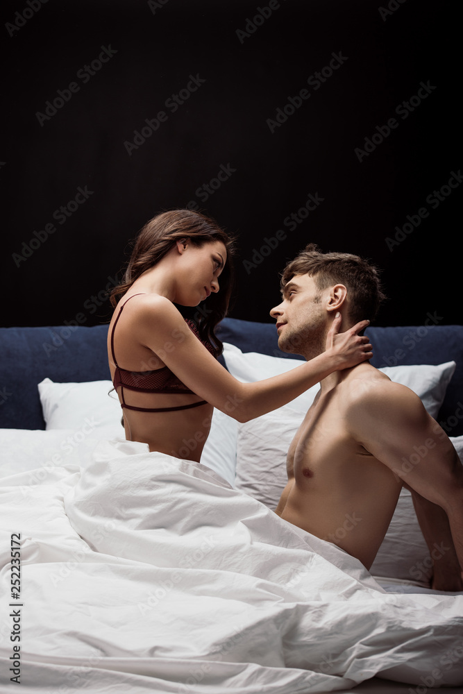 young woman in sexy lingerie embracing man in bed isolated on black young woman in sexy lingerie embracing man in bed isolated on black