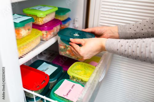 Woman placing container with frozen vegetables in freezer.