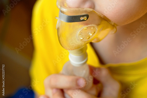 Child closeup makes inhalation at home with nebulizer on out of focus background. photo