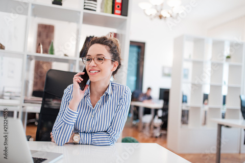 Happy female entrepreneur talking on mobile phone at work. photo