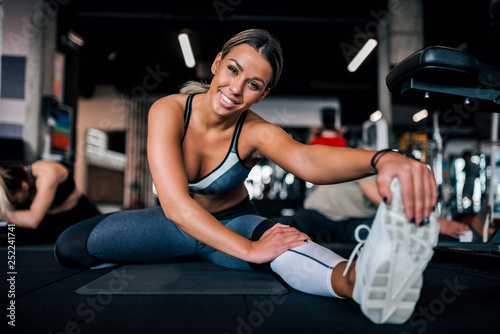 Low angle image of fit woman stretching legs in the gym, smiling at camera.