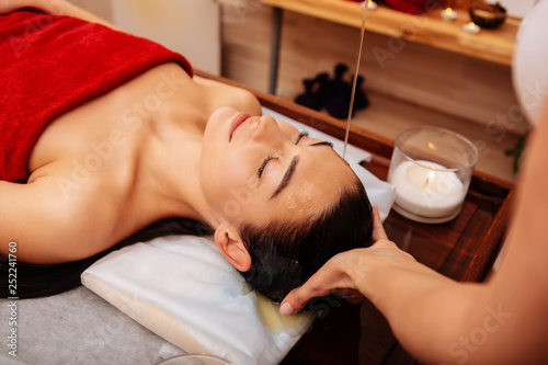 Принти на полотні Dark-haired peaceful young woman feeling all benefits of shirodhara treatment