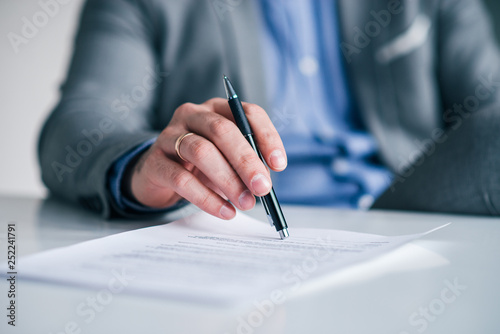Foto Business executive's hand holding pen over the contract, document on the white table, close-up