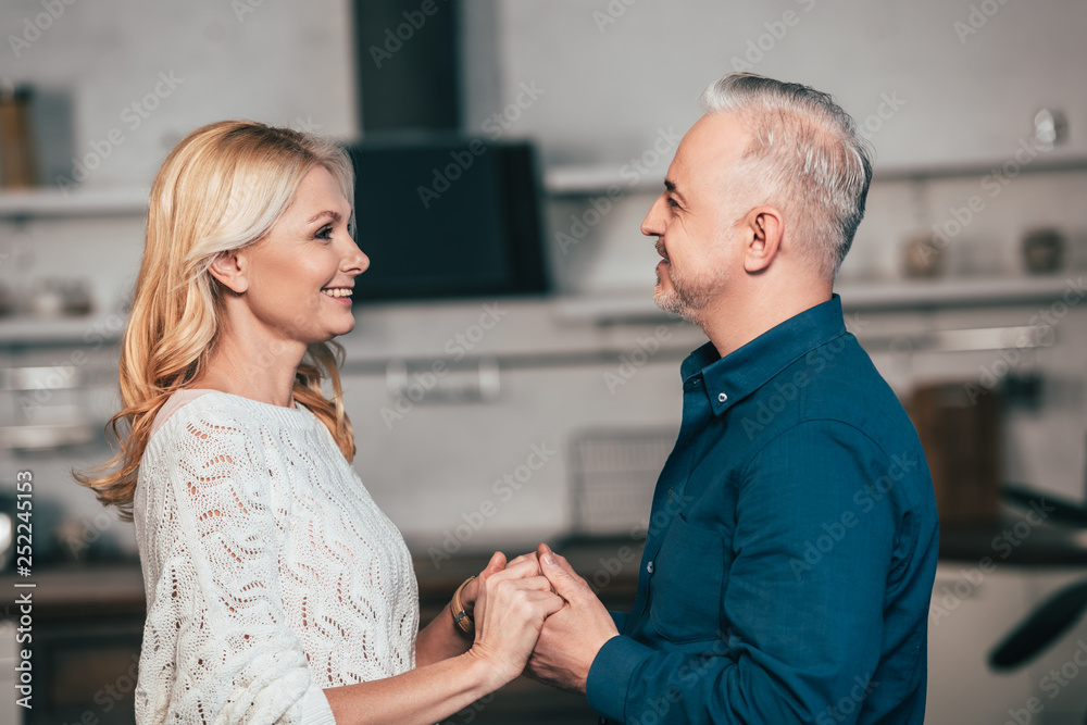 Obraz premium happy wife and husband holding hands and smiling at home