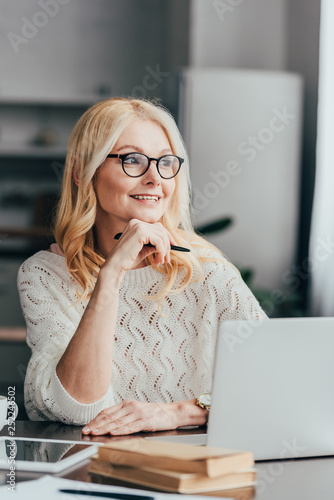 selective focus of cheerful woman in glasses sitting near laptop
