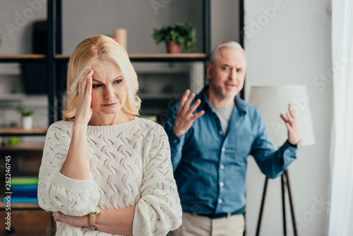 selective focus of woman holding head while husband arguing on background