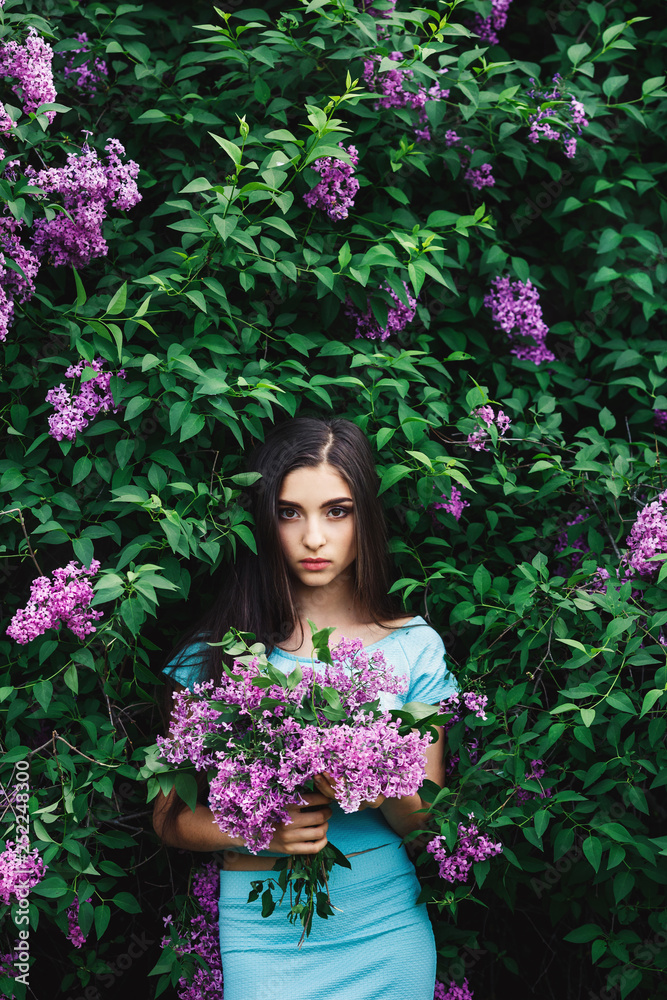 Wonderful spring. Cute young girl enjoys nature among the blossoming lilac and holds a bouquet.