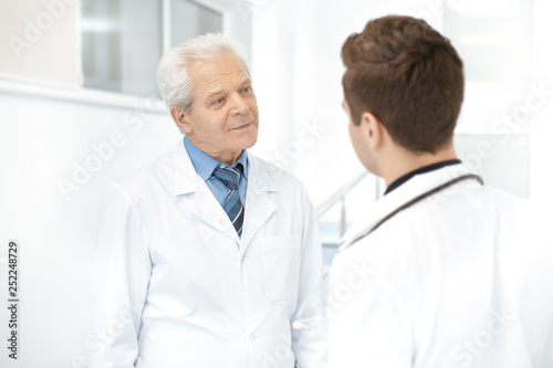 Elderly doctor having a discussion with his younger colleague at the hospital hallway