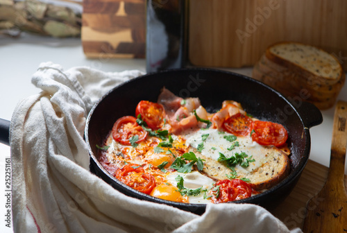 Fried eggs with bacon, toast and tomatoes in a pan