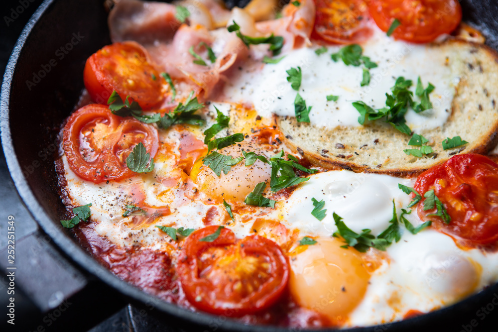 Fried eggs with bacon, toast and tomatoes in a pan