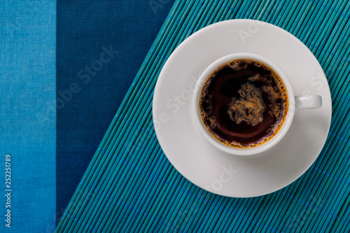 Top view of a black coffee cup on blue bamboo mat and fabric background