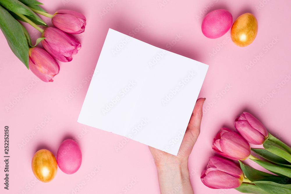 Female hand hold present card on a pink background with flowers and easter eggs