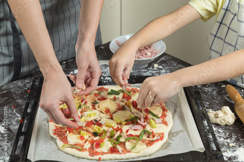 Mother with the child do house pizza. Pizza dough lies on a table. The child puts ingradiyenta on fresh dough