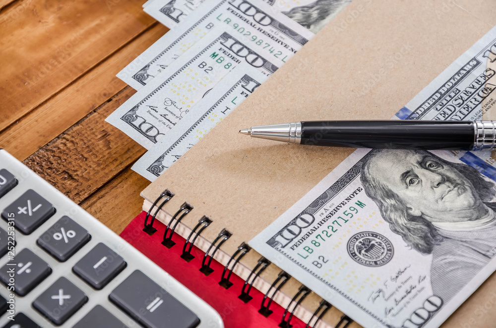 Fototapeta premium American dollars, calculator, pen and notebook on a wooden background