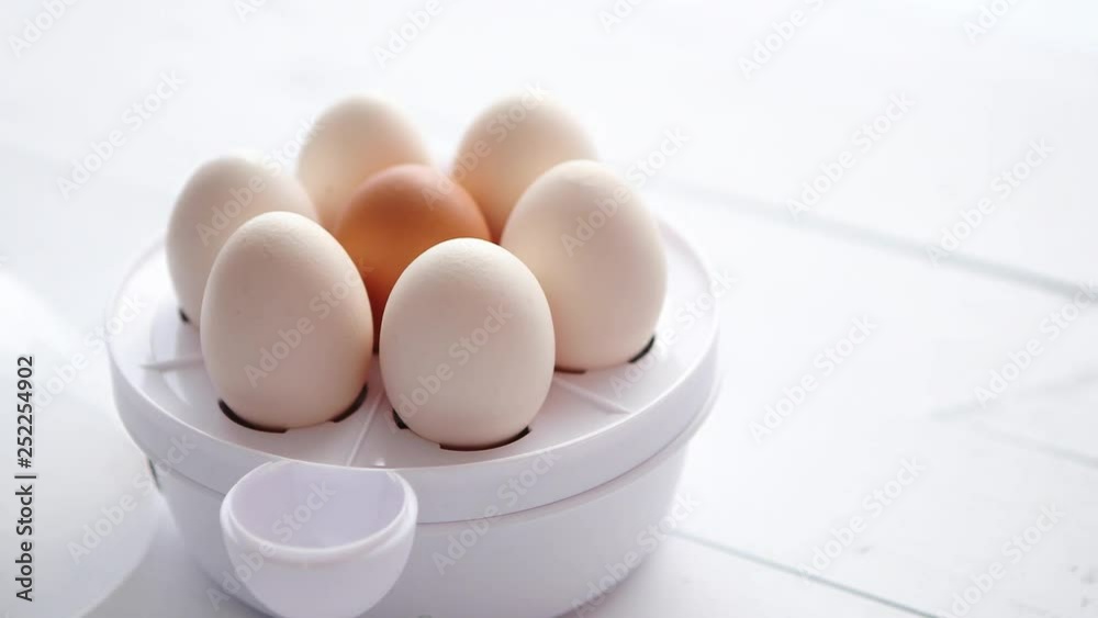 Chicken eggs in a egg electric cooker on a white wooden table Chicken eggs in a egg electric cooker on a white wooden table