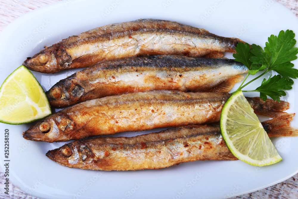 Deep frying small fish capelin and sliced lemon on white plate. Good snack to beer. Deep frying small fish capelin and sliced lemon on white plate. Good snack to beer.