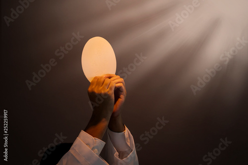 Fotografiet Hands of priest raise sacramental bread under light