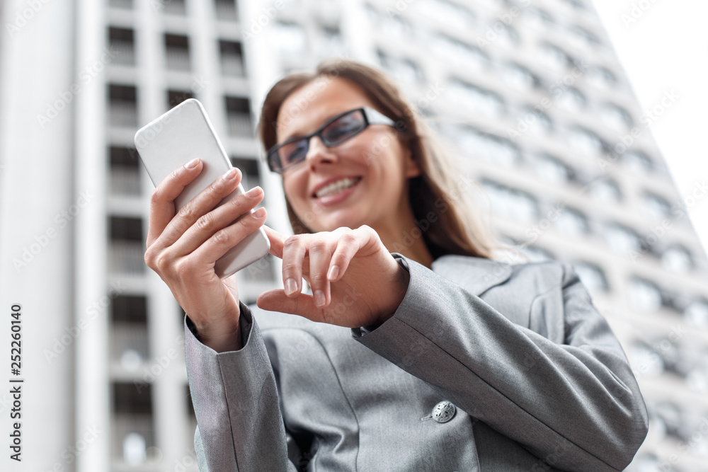 Business woman in eyeglasses standing on the city street using app on smartphone cheerful close-up bottom view