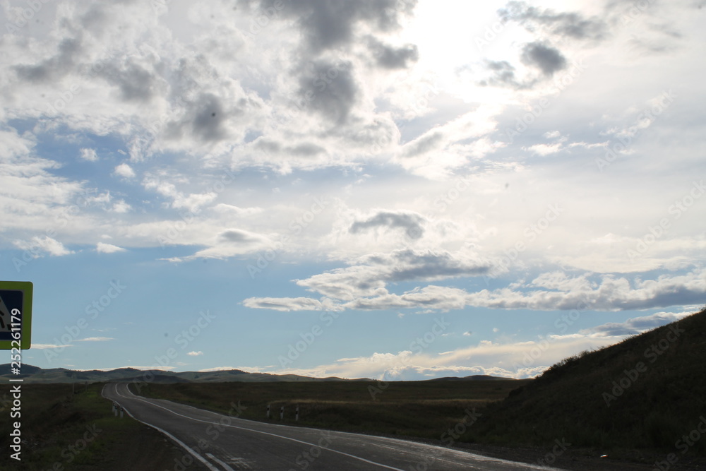 road in steppe under a blue sky with white clouds Sayan mountains Siberia Russia