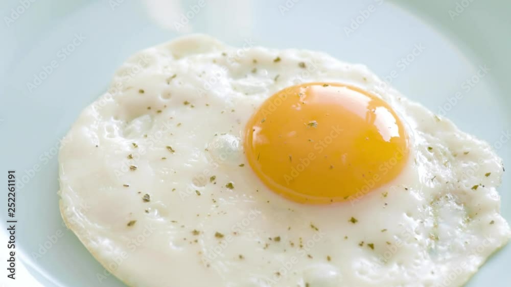 Fried egg with spices are laid out from frying pan on plate. Top view close-up. Fried egg with spices are laid out from frying pan on plate. Top view close-up.