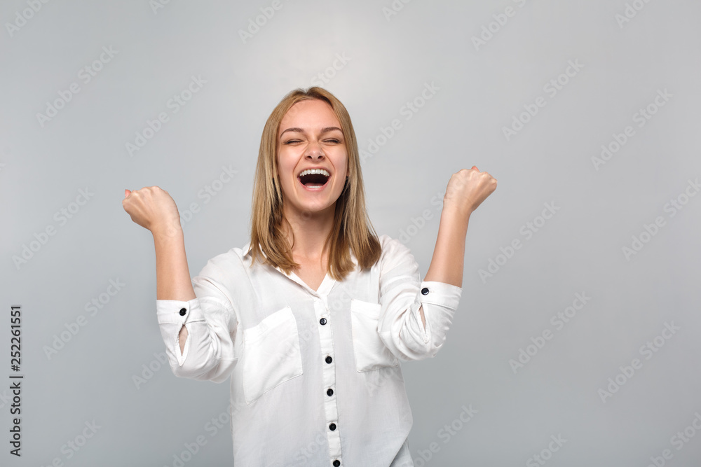 Young woman standing isolated on grey hands up laughing successful Young woman standing isolated on grey hands up laughing successful