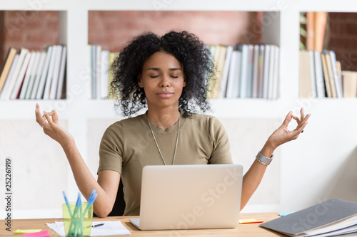 Calm black businesswoman taking break meditating doing yoga at work