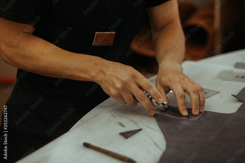 Obraz premium Man holding crafting tool and working. Close up of a master working with leather textile at his workshop using tools. Handmade concept.